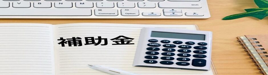 補助金と書かれたノートと電卓、キーボードのあるデスクのイメージ