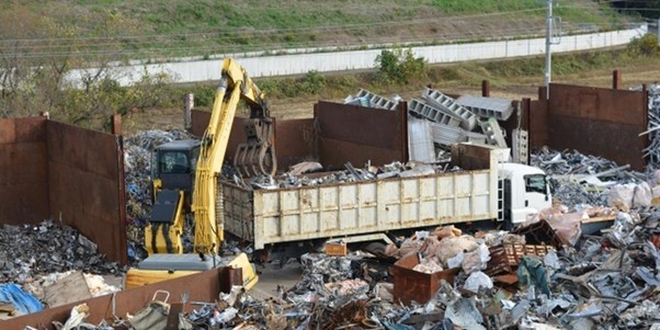 金属スクラップを積み込む作業現場。トラックと重機が廃材を処理中