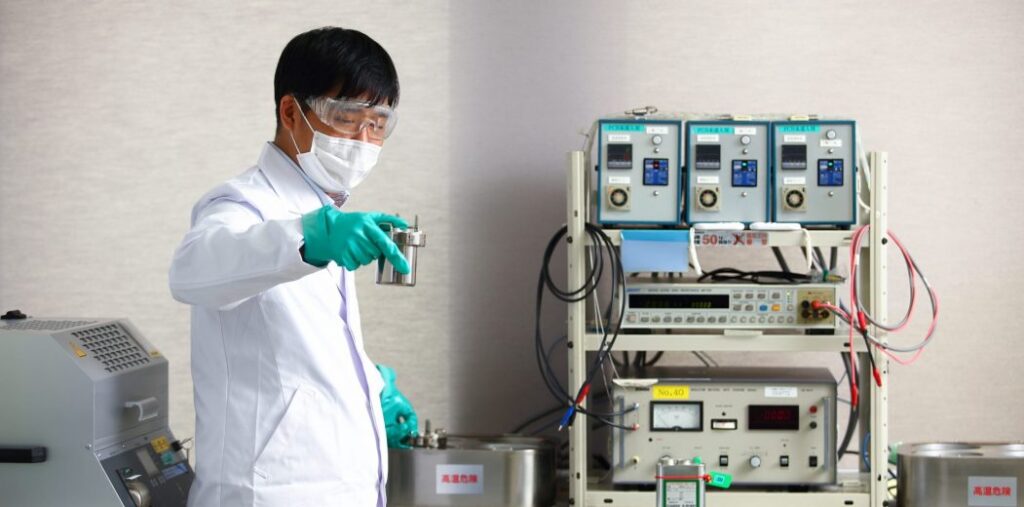 分析設備の前で絶縁油が入った入れ物を持つ男性研究員